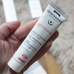 Une main tient un tube de crème anti-rougeurs de la marque Isispharma, contenant de l'acide azélaïque pour apaiser les rougeurs sévères.