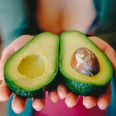Manos sostienen un aguacate cortado por la mitad, listo para comer aguacate todos los días.