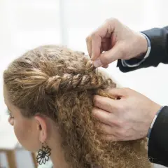 Hårstylist flätar en del av en kvinnas lockiga hår. En bra frisyr kan ge inspiration för hur man får lockigt hår.