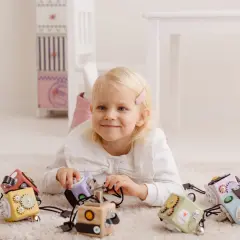 Uśmiechnięta dziewczynka bawi się kolorowymi kostkami manipulacyjnymi drewnianymi na dywanie.