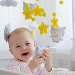 Uśmiechnięte dziecko bawi się wiszącymi zabawkami kontrastowymi od kiedy jest małe. Sowy i gwiazdki zachwycają malucha.