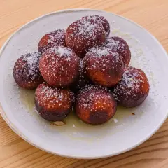 En hög med söta, mörka gulab jamun, pudrade med kokosflingor och serverade i en ljus sirap.