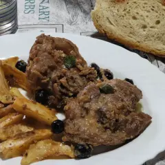 Un saporito ossobuco di tacchino con patate arrosto e olive nere, accompagnato da pane fresco e un bicchiere di vino bianco.