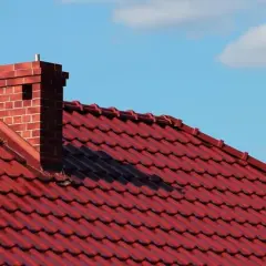 Roter Ziegeldach mit einem gemauerten Kamin. Die Anschlussstelle zwischen Kamin und Dach scheint undicht zu sein.