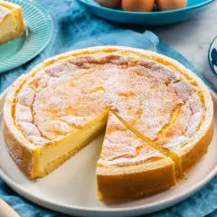 Torta soffice e dorata, simile a un quark formaggio, cosparsa di zucchero a velo. Una fetta è già servita.