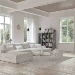 Soggiorno luminoso con divano bianco, libreria e finestre ampie. Un esempio di come dipingere una stanza per farla sembrare più grande, usando colori chiari e arredi minimalisti.