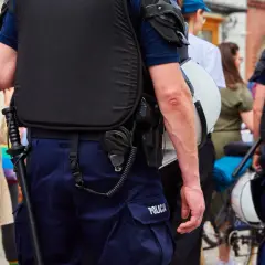 Funkcjonariusz publiczny w kamizelce taktycznej i mundurze, z pałką i kajdankami, stoi na straży porządku.