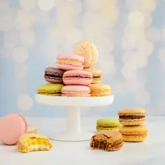 Bunte Macarons, frisch gebacken, stapeln sich auf einem weißen Tortenständer. Einige sind angeknabbert und zeigen ihre cremige Füllung.