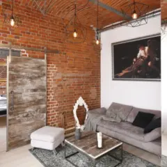 Nowoczesny salon z odsłoniętą, starą cegłą na ścianie. Wygodna sofa, stolik kawowy i przesuwne drzwi dodają charakteru.