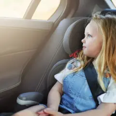 Ein blondes Mädchen sitzt im Kindersitz und schaut aus dem Fenster. Die Frage "wie lange Kindersitz" beschäftigt viele Eltern.