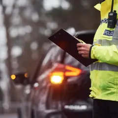 Policjant w kamizelce odblaskowej z napisem "POLICE" spisuje mandaty na Słowacji. W tle widać samochód z włączonymi światłami awaryjnymi.