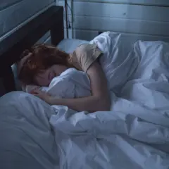 Una persona duerme profundamente, envuelta en sábanas blancas, quizás soñar con espíritus en la penumbra de la habitación.