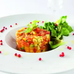 Délicieux tartare de truite aux agrumes, avocat et poivrons, garni de jeunes pousses et de baies roses sur une assiette blanche.
