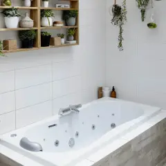 Baignoire d'angle avec robinetterie chromée. La hauteur du robinet baignoire est idéale pour remplir la vasque. Des plantes décorent l'espace.