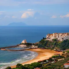 Vue d'une ville côtière italienne perchée sur une falaise, avec une plage et un port en contrebas.