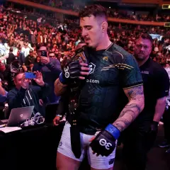 Mistrz UFC z pasem na ramieniu, otoczony tłumem fanów robiących zdjęcia.