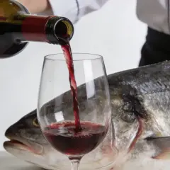 Un chef verse du vin rouge dans un verre, à côté d'un poisson entier. Une question se pose : quel vin rouge avec du poisson ?