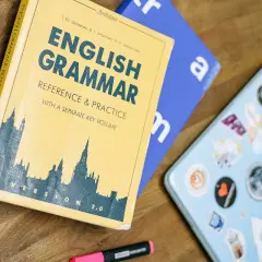 Książka "English Grammar: Reference & Practice" i niebieski notatnik leżą na drewnianym blacie. Idealne do nauki zadań gramatycznych angielskiego.