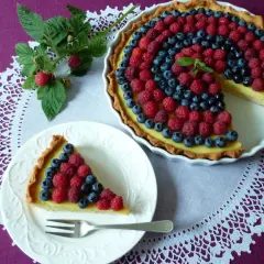 Letnia tarta z kremem budyniowym, ozdobiona malinami i borówkami, kusi apetycznym wyglądem.