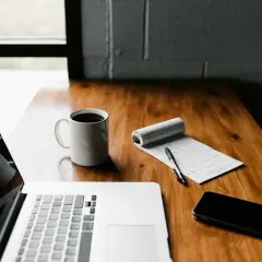 Laptop, kawa, notatnik z długopisem i telefon na drewnianym biurku. Płatnik przygotowuje się do pracy.