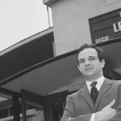 Jean Pierre Léaud w garniturze, z rękami skrzyżowanymi na piersi, przed budynkiem z napisem "Le Beau Serge".