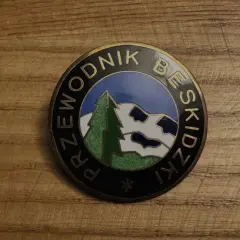 Odznaka z napisem "Przewodnik Beskidzki" i malowniczym krajobrazem górskim.