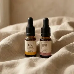 Två flaskor ansiktsolja med pipett på en beige duk. Oljorna innehåller e-vitamin hudvård för en strålande hy.