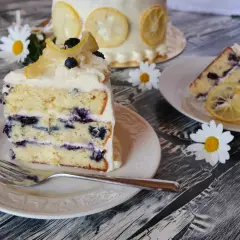 Ein Stück saftiger Zitronen-Blaubeerkuchen mit cremigem Frosting, garniert mit kandierten Zitronenscheiben und frischen Blaubeeren.