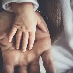Dłoń dorosłego obejmuje dłoń niemowlęcia. To symbol opieki nad zdrowym dzieckiem, czułości i bezpieczeństwa.