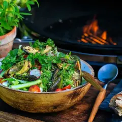 En stor skål med god sallad, grillad aubergine och sparris, med en grill i bakgrunden. Perfekt för en sommarkväll.
