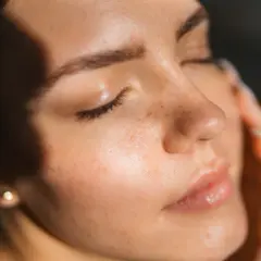 Viso di donna con lentiggini, illuminato da luce soffusa. La pelle appare curata, suggerendo che retinolo e vitamina C si possono usare insieme per un incarnato radioso.