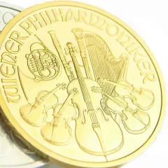 Złota moneta z instrumentami muzycznymi, w tym skrzypcami i harfą. Napis "Wiener Philharmoniker" otacza scenę.