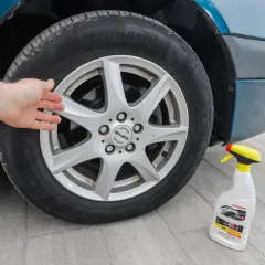 Dłoń dotyka felgi aluminiowej, obok stoi butelka z płynem do czyszczenia felg.