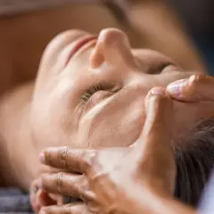 Mani esperte dimostrano come massaggiare il viso per le rughe, con un tocco delicato sulla fronte e sulle tempie per un effetto rilassante e ringiovanente.