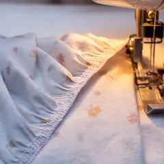 A serger creates a gathered edge on a floral-patterned fabric, preparing it for a sewing project.
