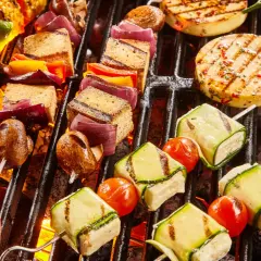 Bunte Spieße mit Tofu, Zucchini, Tomaten, Mais und Paprika brutzeln auf dem Grill. Ein Genuss für vegetarisches Grillen!