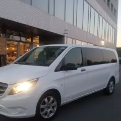 Biały bus przed hotelem Arche. Sprawdź nasz wynajem busa z kierowcą cennik dla komfortowych podróży.