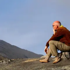 A man in hiking gear sits on a rock, contemplating the vast, barren landscape. This is the essence of zero day hiking, a moment of quiet reflection before the real adventure begins.