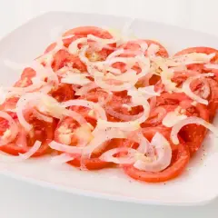 Una refrescante ensalada de tomate y cebolla, aderezada con sal y pimienta, lista para disfrutar.