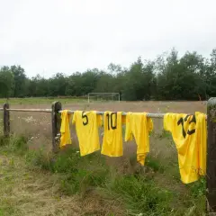 Maillots de foot jaunes floqués, numéros 5, 10, 12, sèchent sur une barre rouillée. Une astuce pour savoir comment laver un maillot de foot floqué.