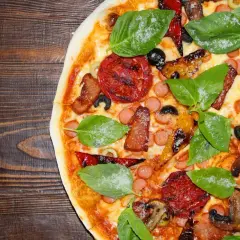 Pyszne rodzaje pizzy: z pomidorami, kiełbaską, boczkiem, oliwkami i bazylią na drewnianym blacie.
