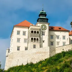 Zamek na Pieskowej Skale, biały z czerwonym dachem, z wieżą zegarową, na tle błękitnego nieba.