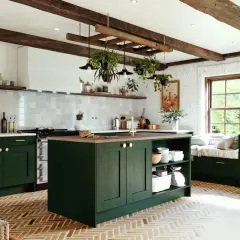 A rustic DIY kitchen remodel cost is managed with dark green cabinets, exposed beams, and a herringbone floor.