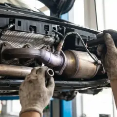 Mechanik wymienia katalizator w Oplu p0420. Widoczny układ wydechowy i ręce w rękawicach.