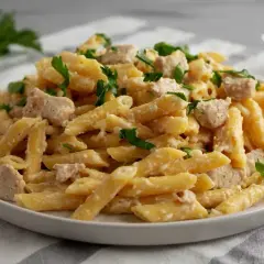 Penne z kurczakiem w kremowym sosie mascarpone, posypane świeżą natką pietruszki. Pyszne danie gotowe do podania.