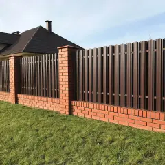 Solidne, wysokie ogrodzenie od sąsiada z cegły i brązowego metalu, chroniące zielony trawnik i dom.
