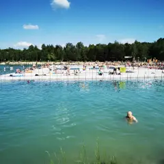 Słoneczny dzień nad jeziorem w Trzebini. Ludzie odpoczywają na pomoście i kąpią się w turkusowej wodzie.