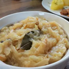 Pyszna kapusta kiszona zasmażana z liściem laurowym i zielem angielskim, podana w białej miseczce.
