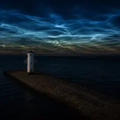 Latarnia morska na kamiennym falochronie, nocne obłoki na niebie. Niesamowita przyroda nad morzem.