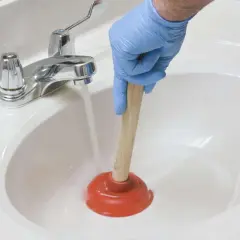 Main tenant utilise une ventouse pour déboucher un lavabo. L'eau s'accumule, signe d'un lavabo bouché.